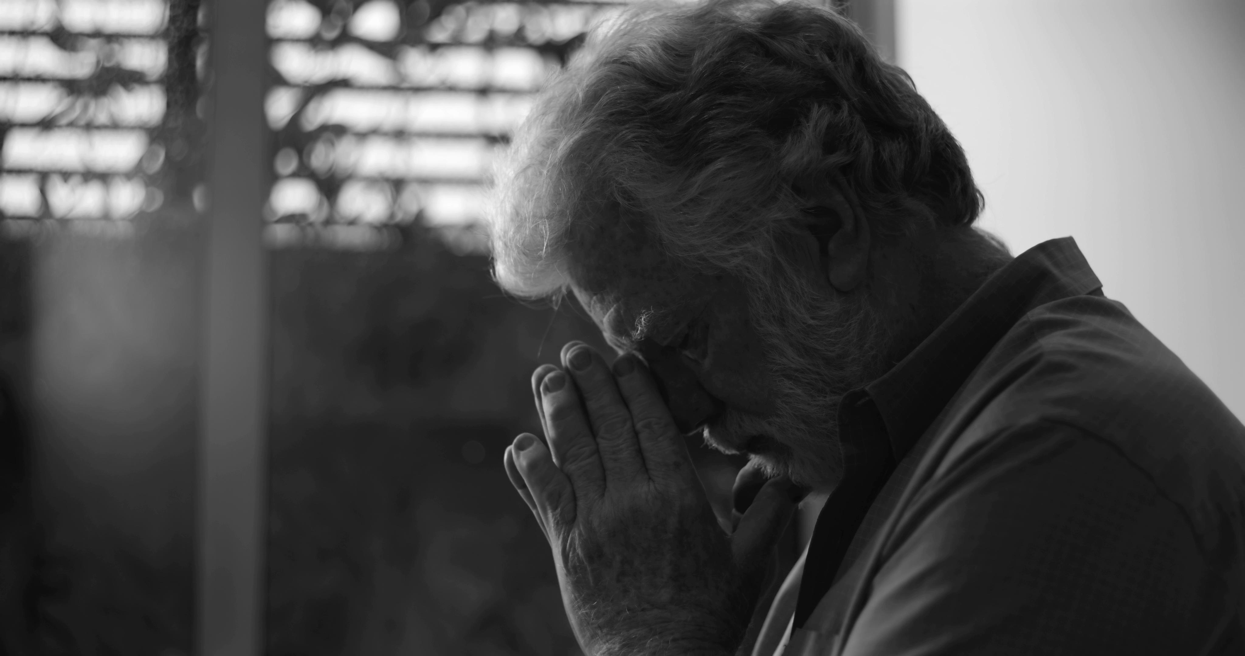 An elderly man with gray hair holds his face in his hands in a contemplative pose, photographed in black and white. An elderly man with gray hair holds his face in his hands in a contemplative pose, photographed in black and white.