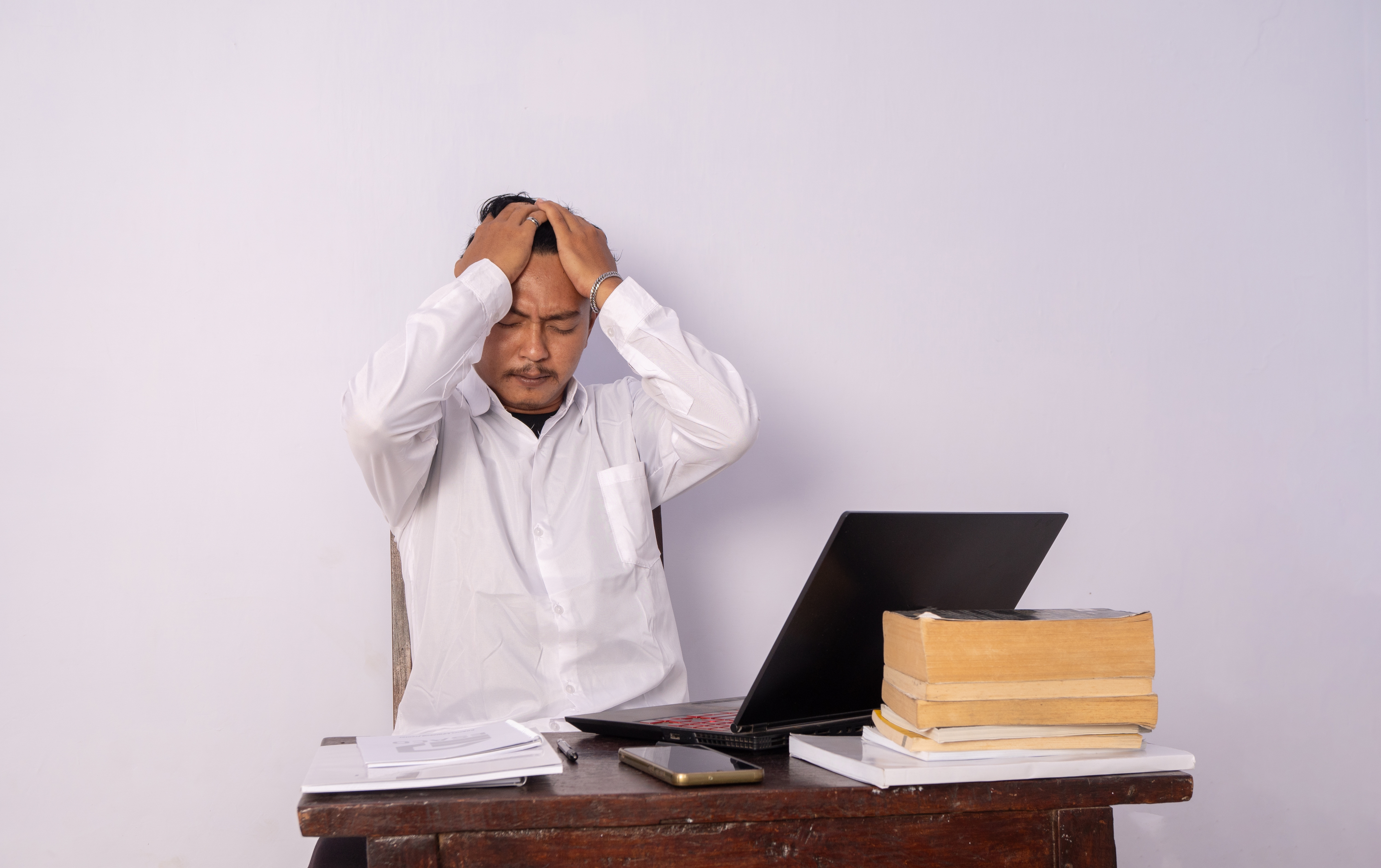 Stressed man with hands on his head sitting at a desk with a laptop Stressed man with hands on his head sitting at a desk with a laptop