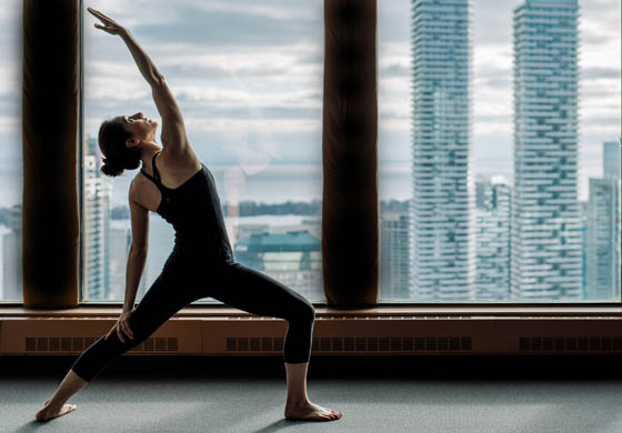 Female member doing a warrior pose in the Strength Lab at the Toronto Athletic Club. Incredible skyline view of the city and the lake in the background.