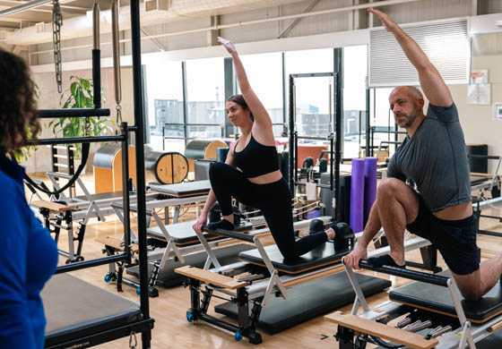 Young woman and middle aged man doing a Pilates class on the reformers in the Pilates loft at the Toronto Athletic Club with an expert instructor guiding them