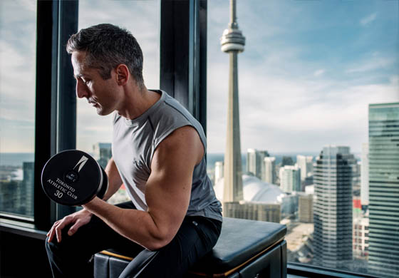 Middle aged fit man lifting a dumbbell in the Toronto Athletic Club in front of the CN Tower