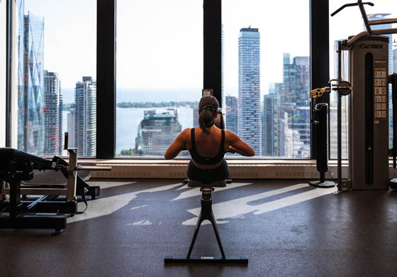 Back of a strong woman on the rowing machine in the Strength Lab at the Toronto Athletic Club, view overlooking the lake and city