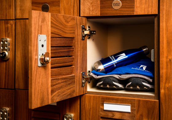 Close-up of a wooden locker at the Toronto Athletic Club with a branded water bottle, folded clothes, and running shoes inside