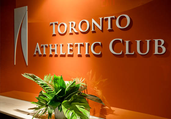 Close-up of orange wall behind the reception desk at the Toronto Athletic Club with the Club's logo and a plant