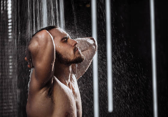 Man showering in a black tiled shower, head thrown back