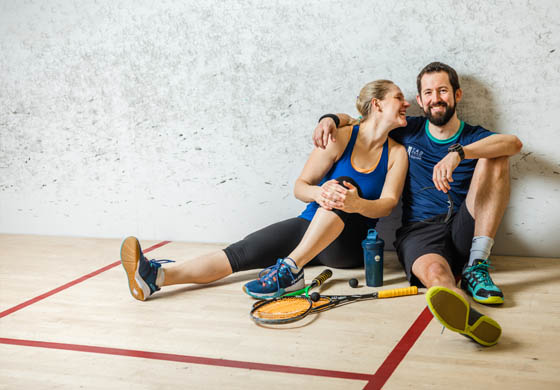 Man and woman - married couple - cozy up on the squash courts at the Toronto Athletic Club with their racquets, waters, and balls on the court in front of them