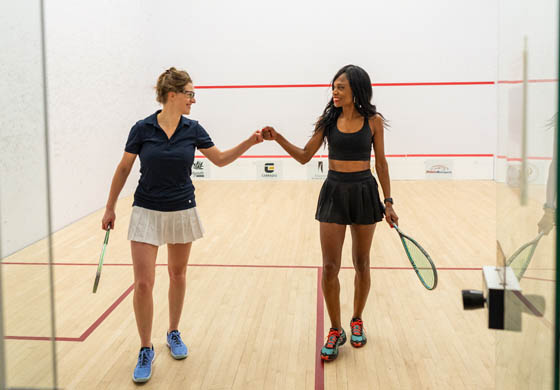 Two middle aged, fit women celebrating as they walk off the squash court at the Toronto Athletic Club