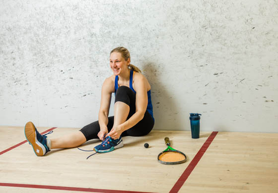 Young fit woman sitting on the squash court at the Toronto Athletic Club, tying her shoes with racquet and balls beside her