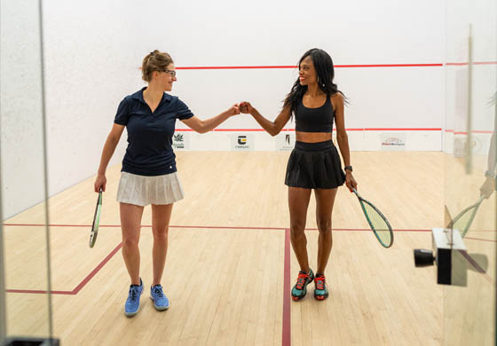 2 middle aged women fist bumping on their way off the squash court at the Toronto Athletic Club