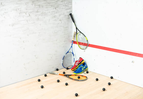 3 squash racquets, pair of shoes, and squash balls spread out in the corner of the court