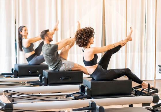 Three young, fit people (2 women and a man) doing a Pilates workout on reformers in a studio