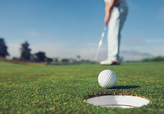 Close-up of golf ball on a putting green, man putting in the background