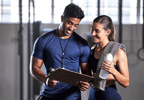 Young male trainer meeting with young female client, looking at a clipboard during a training session