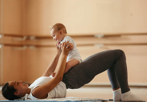 New, young mom doing a bridge with her baby sitting on her pelvis